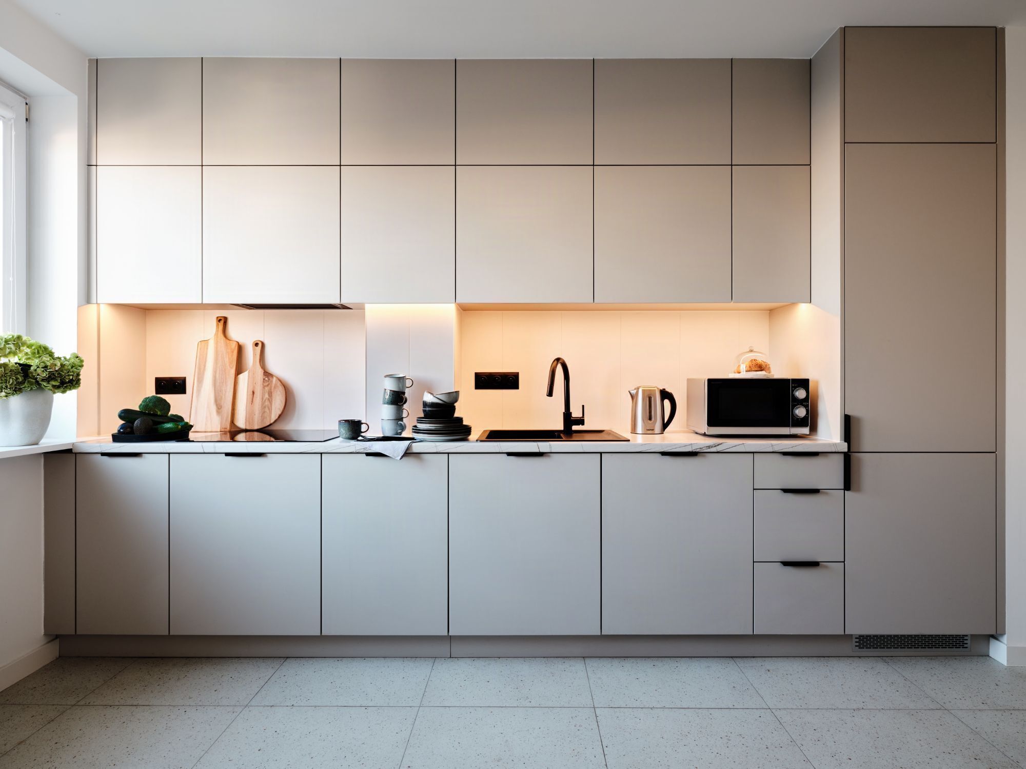 Une cuisine moderne avec des meubles blancs, un évier en acier inoxydable et un four à micro-ondes.
