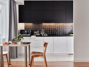 A modern kitchen with black cabinets, a microwave, and a dining area with a table and chairs. - Media Park (Warsaw)