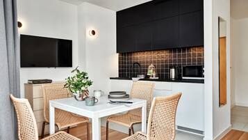 A modern kitchen with a dining area, featuring a flat-screen TV, black cabinets, and a tiled backsplash.