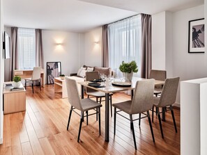 A modern dining area with a wooden table, grey upholstered chairs, and a potted plant. - Media Park (Warsaw)