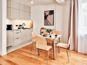A modern kitchen with white cabinets, a dining area with a table and chairs, and a large window with curtains. - Media Park (Warsaw)