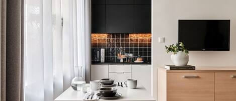 Cozinha moderna com mesa de jantar posta para dois, máquina de café e televisão fixada na parede.
