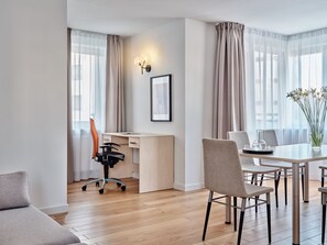 A modern hotel room with a wooden floor, a desk with a chair, a dining table with chairs, and a vase with flowers. - Media Park (Warsaw)