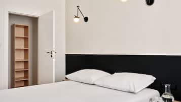 Un dormitorio minimalista con cama, dos lámparas de noche, una mesita de noche con un libro y gafas, y un armario de madera.