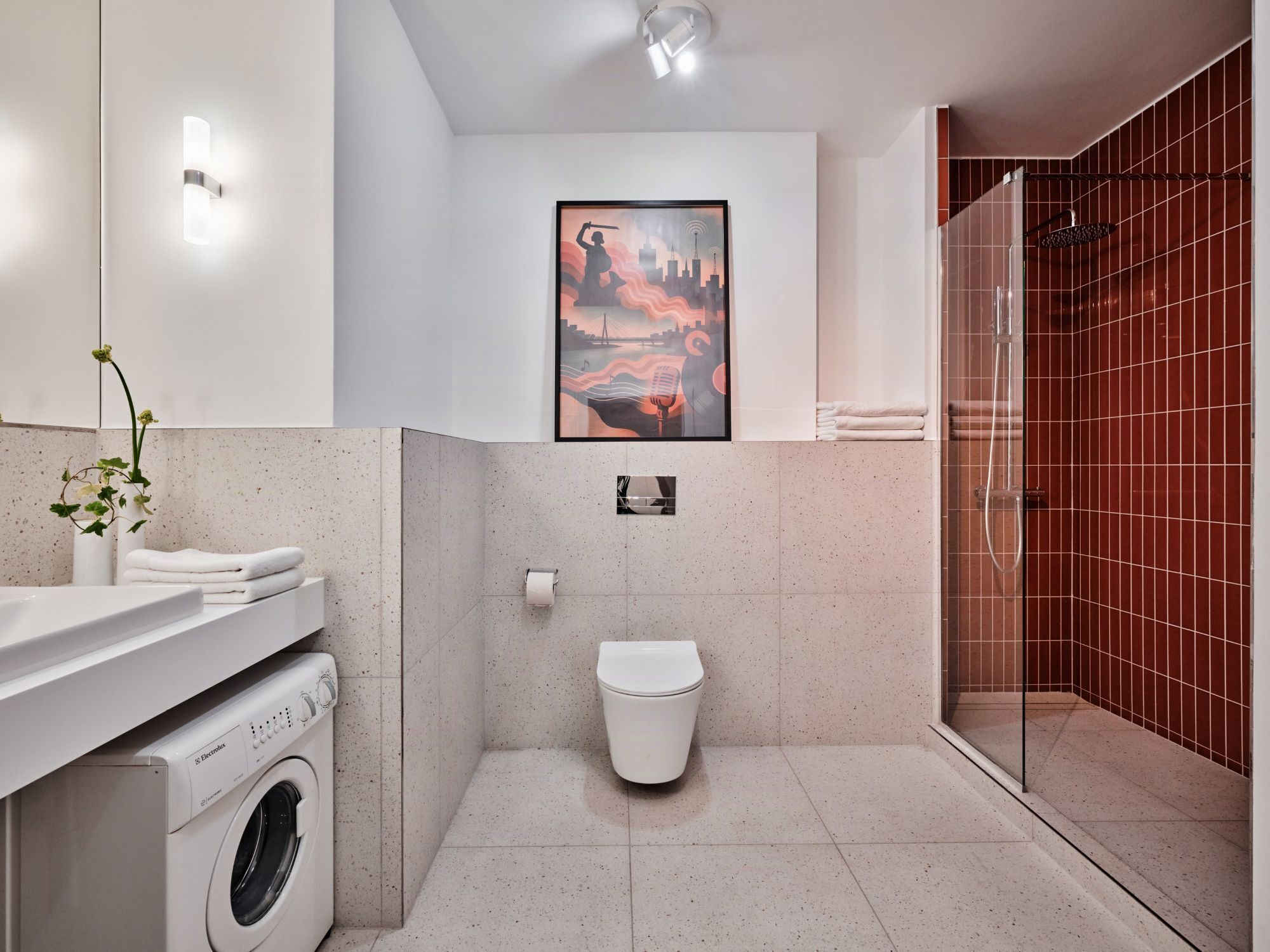 Un baño moderno con ducha, inodoro, lavadora y un cuadro en la pared.