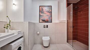 Ein modernes Badezimmer mit Dusche, Toilette, Waschmaschine und einem gerahmten Kunstwerk an der Wand.