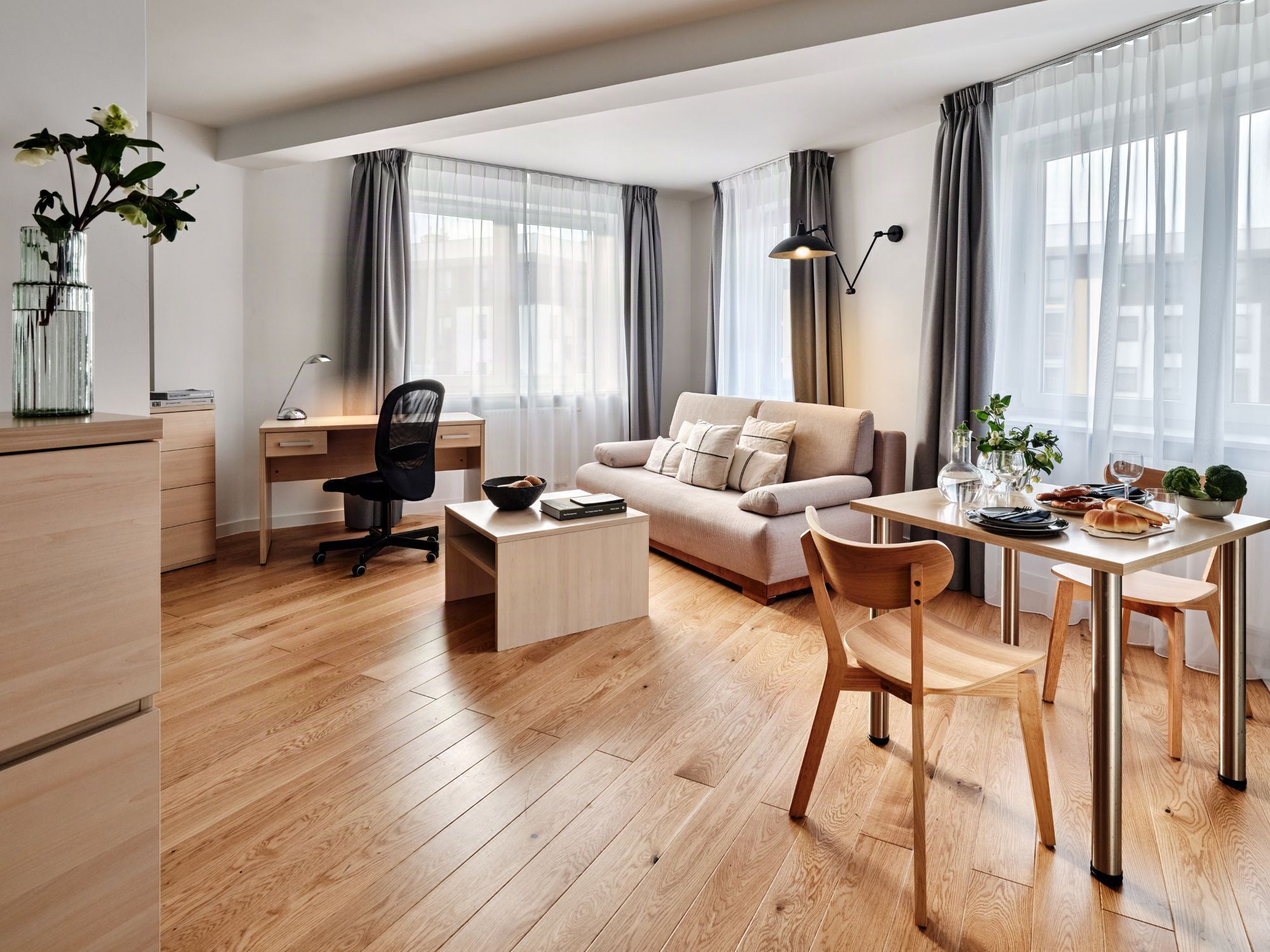 A modern living room with a sofa, coffee table, dining table, and a workspace with a chair and desk.
