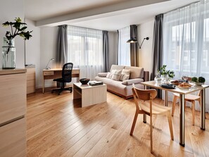 A modern living room with a sofa, coffee table, dining table, and a workspace with a chair and desk. - Media Park (Warsaw)