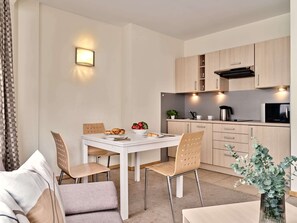 A modern kitchen with white cabinets, a dining table with chairs, and a small dining area with a sofa. - Media Park (Warsaw)