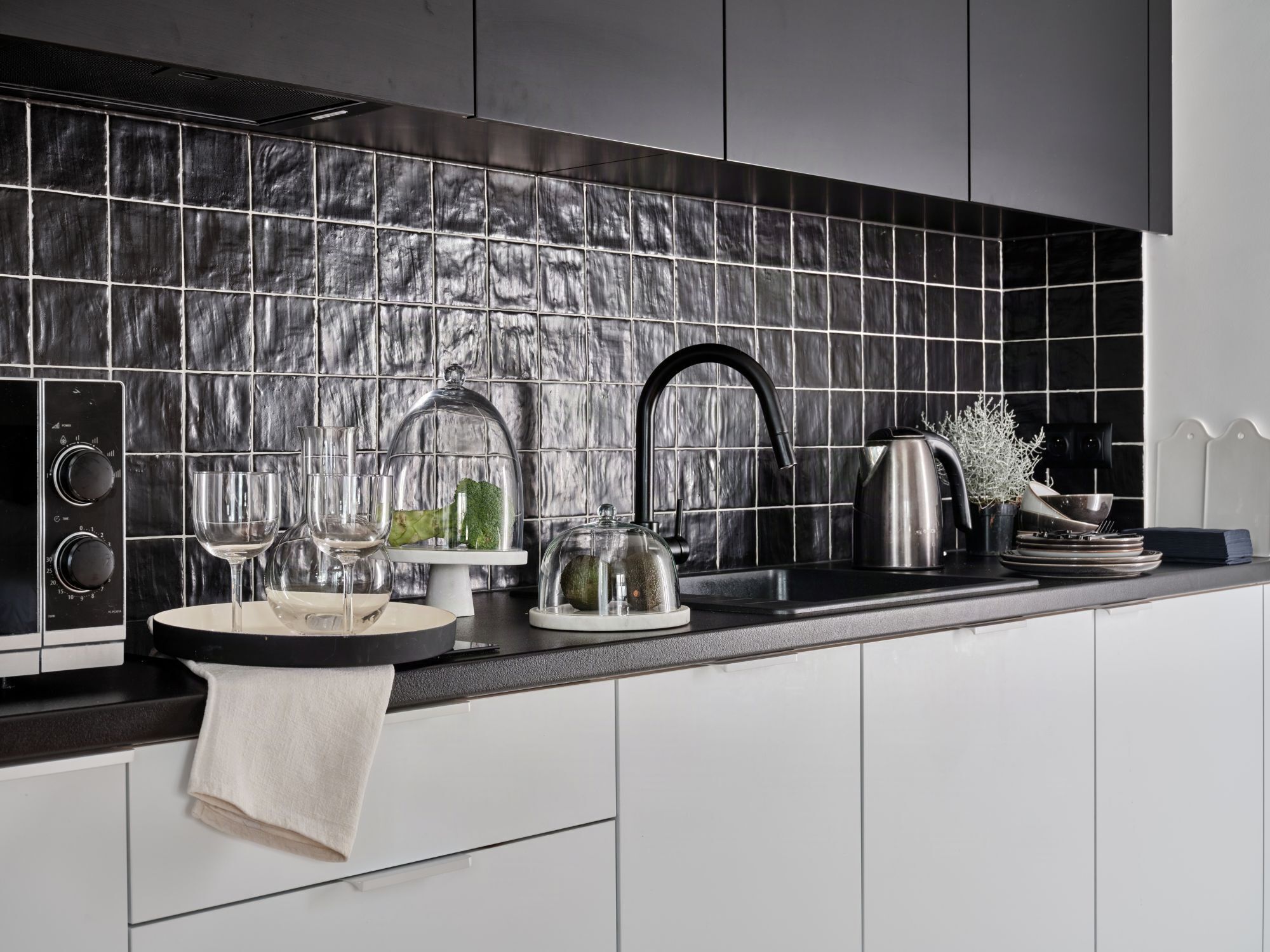 A modern kitchen with a black tiled backsplash, stainless steel appliances, and a white countertop.