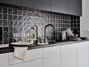 Una cocina moderna con salpicadero de azulejos negros, electrodomésticos de acero inoxidable y encimera blanca.