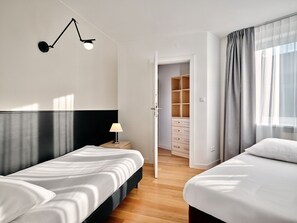 A hotel room with two beds, a bedside table with a lamp, a wardrobe, and a door leading to a bathroom. - Media Park (Warsaw)
