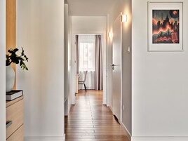 Un corridoio con pavimento in legno, una sedia e una porta che conduce ad un'altra stanza.