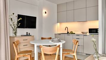 A modern kitchen with a flat-screen TV, wooden chairs, and a dining table.