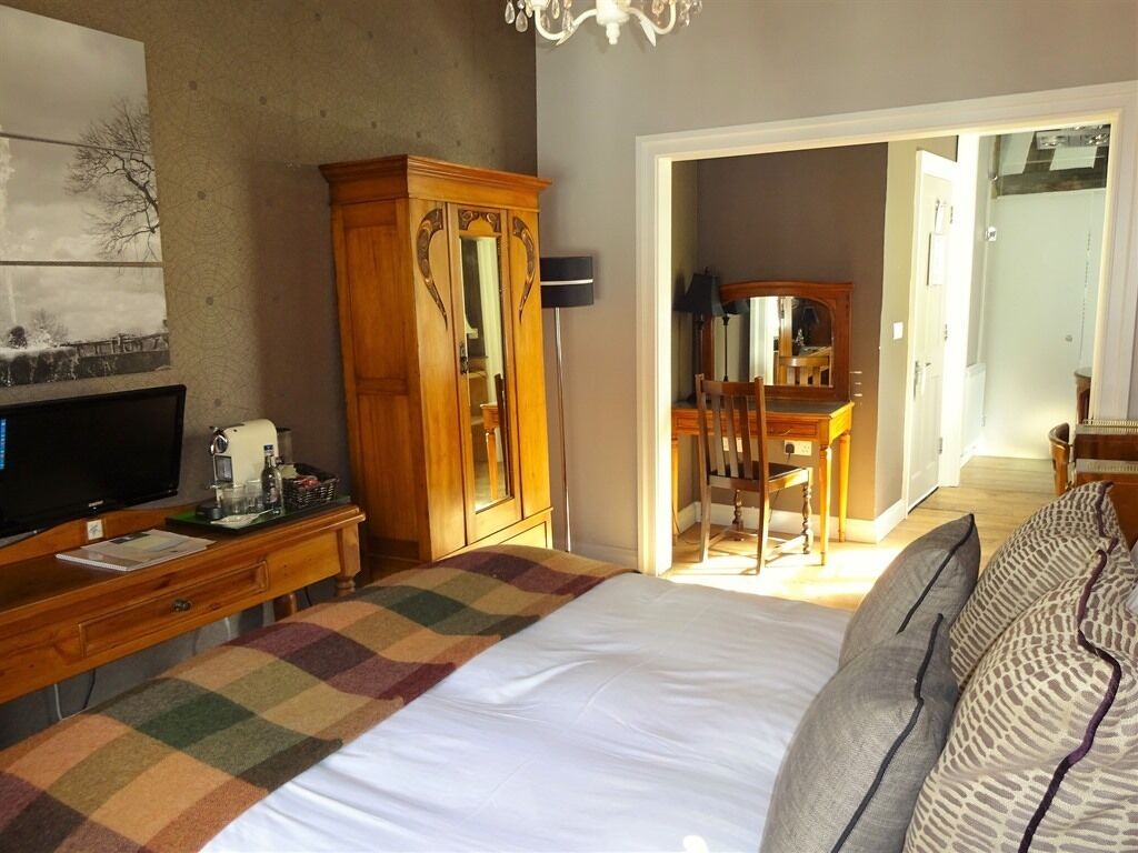 A bedroom with a bed, a wooden wardrobe, a television, and a desk with a chair.