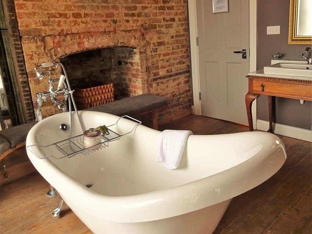 A bathroom with a freestanding bathtub, a wooden bench, a brick fireplace, and a wooden vanity with a mirror.