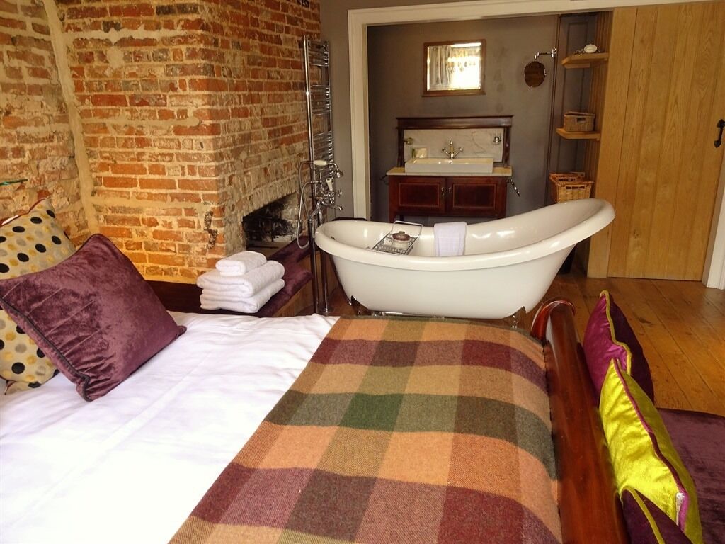 Una habitación con colcha a cuadros, una bañera blanca, pared de ladrillo y una puerta de madera.