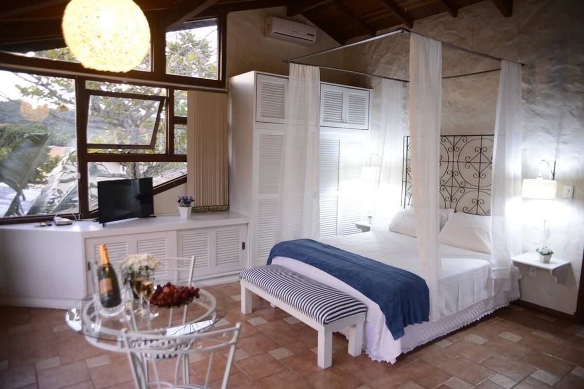 A bedroom with a four-poster bed, a desk with a computer and a bottle of champagne, and a small table with a bottle and fruit.