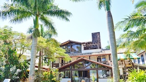 A two-story building with a covered patio area, surrounded by palm trees and various plants. - Encantos da Ilha Pousada (Florianópolis)