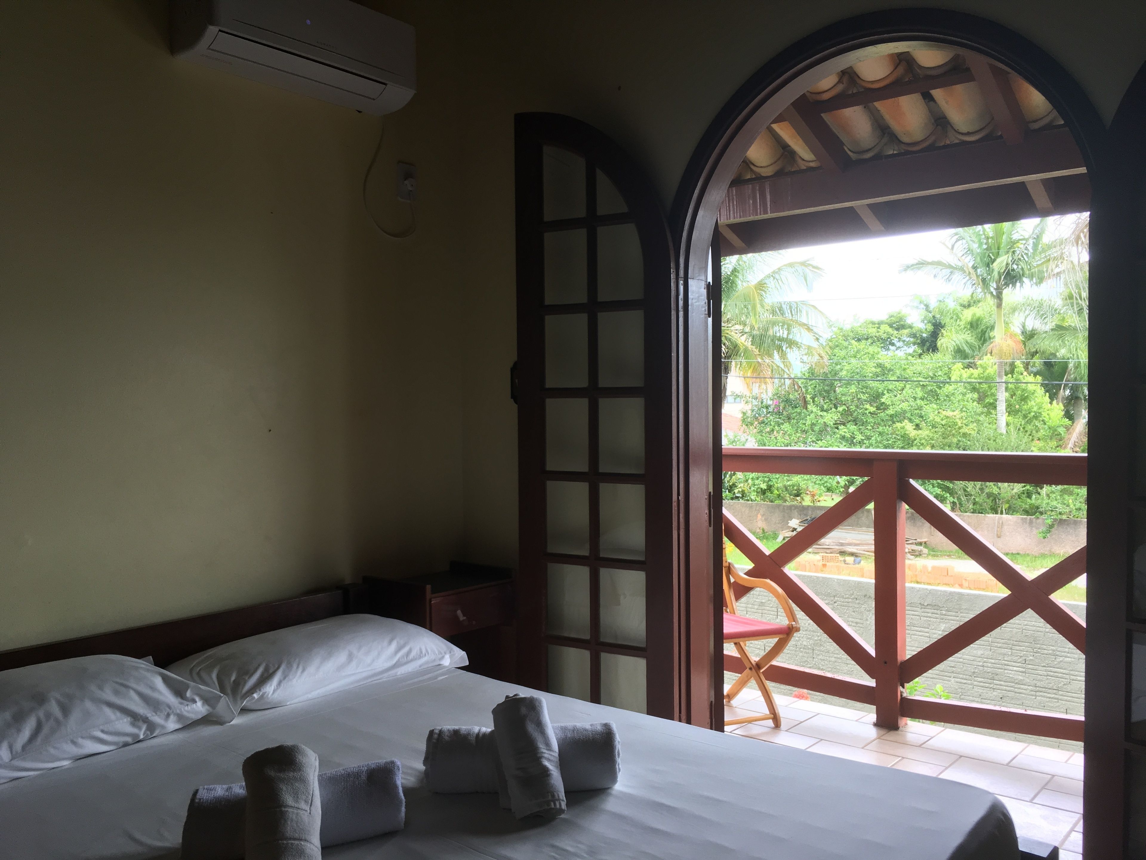 Una camera d'albergo con un letto, una finestra vista verde e un condizionatore.