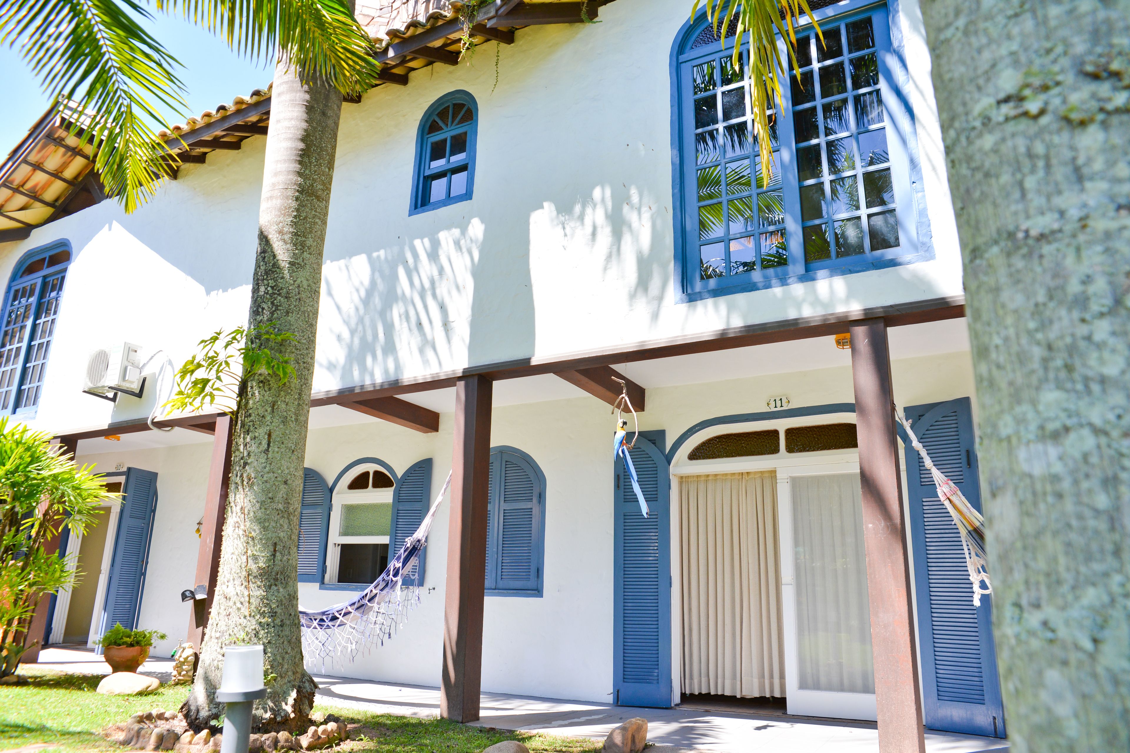 A white building with blue shutters and a hammock hanging from the porch.