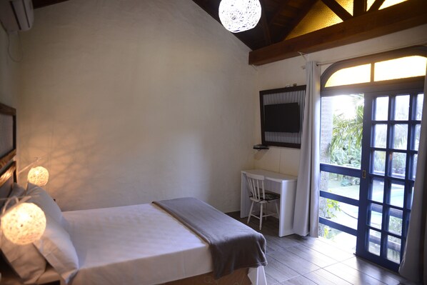 A bedroom with a bed, a desk, and a chair. There is a window with a view of greenery outside.