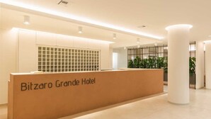 Un comptoir d’accueil à l’hôtel Bitzaro Grande, doté d’un design moderne, avec une grande colonne et une plante en arrière-plan.