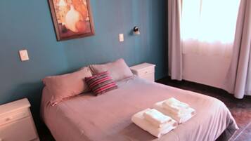 Una camera da letto con un letto, cuscini, un comodino, un quadro e una finestra con tende.