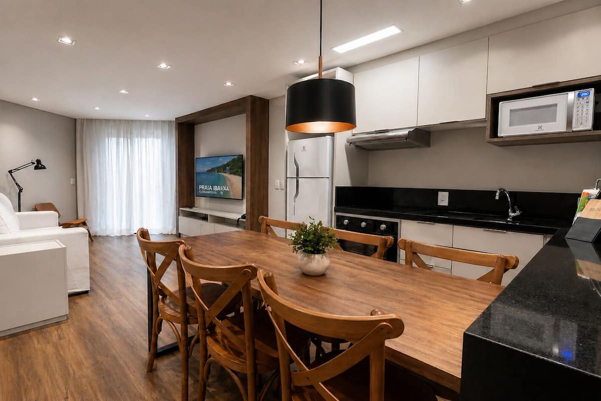 Une cuisine moderne avec un coin repas, des meubles blancs, un plan de travail noir et un téléviseur à écran plat.
