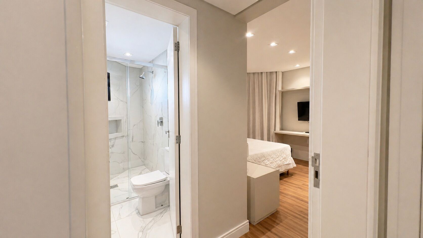 A modern bathroom with a glass shower enclosure, a toilet, and a bed with a white bedspread.