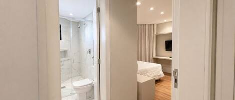 A modern bathroom with a glass shower enclosure, a toilet, and a bed with a white bedspread.
