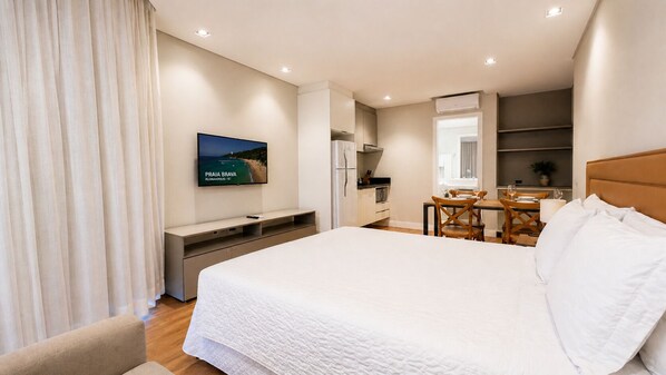 Habitación de hotel con cama, escritorio, mesa de comedor y televisor mostrando una escena de playa.