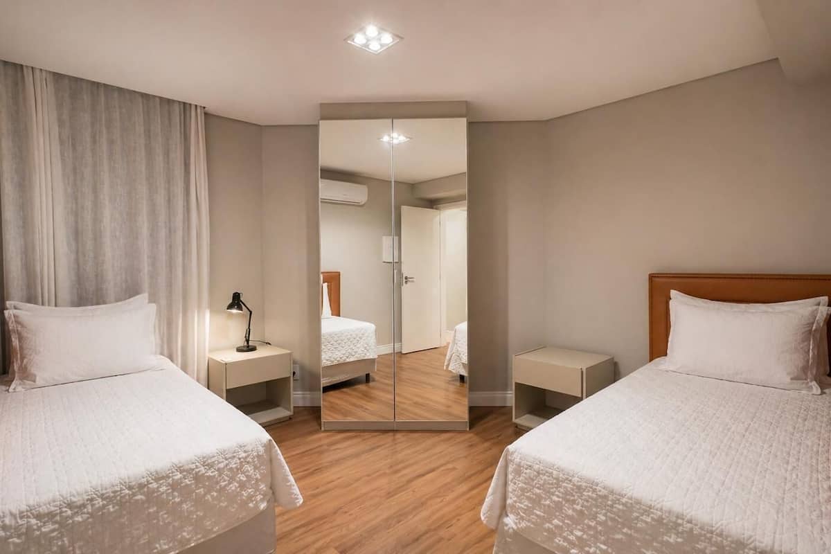 Habitación de hotel con dos camas, un espejo, un escritorio y una mesita de noche.