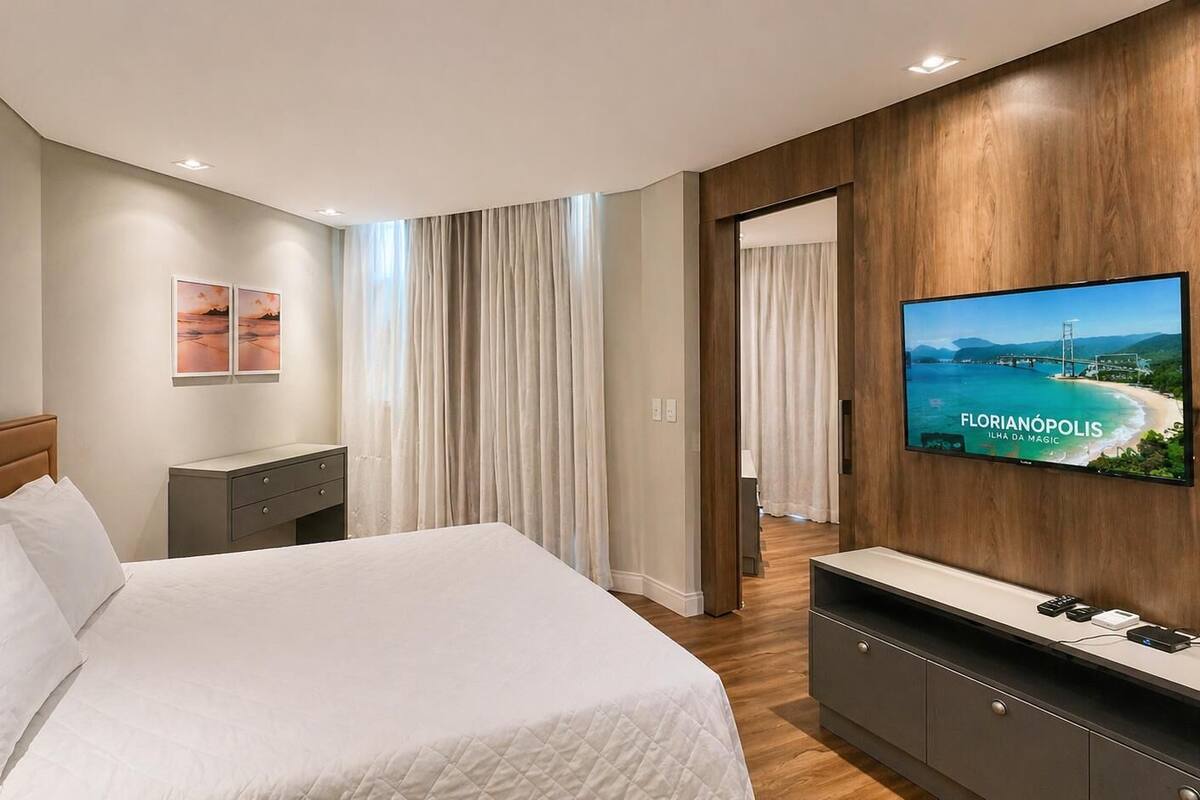 Habitación de hotel moderna con una cama grande, televisión, escritorio y vistas a un paisaje costero.