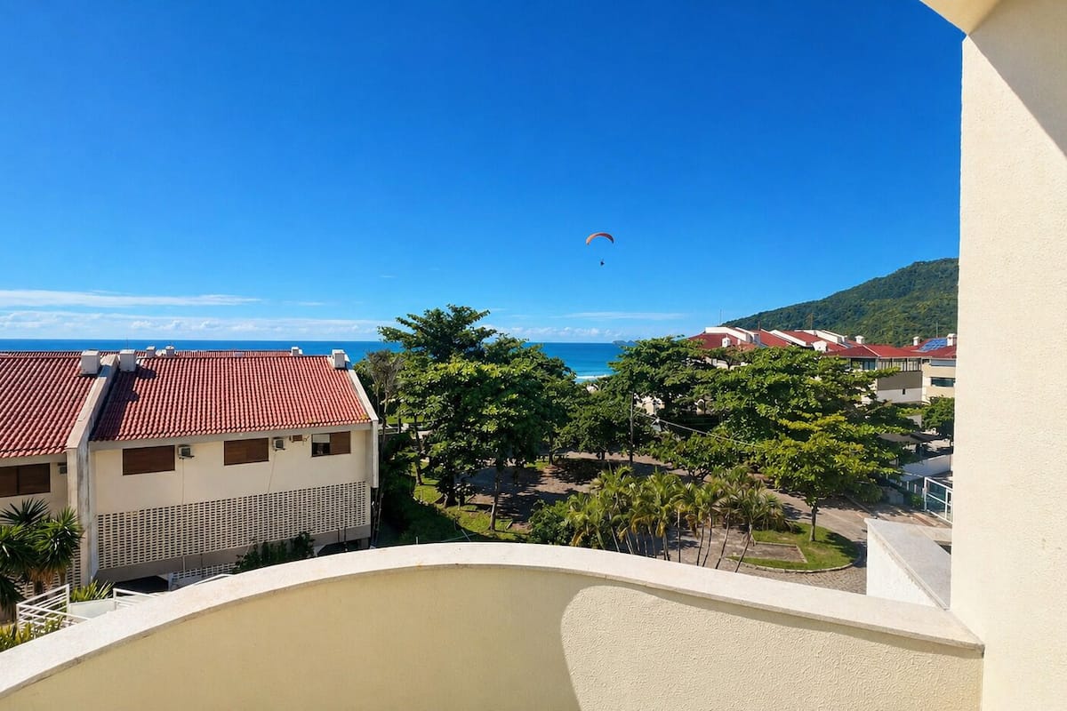 Un balcon donnant sur une plage, des palmiers et des bâtiments aux toits rouges.
