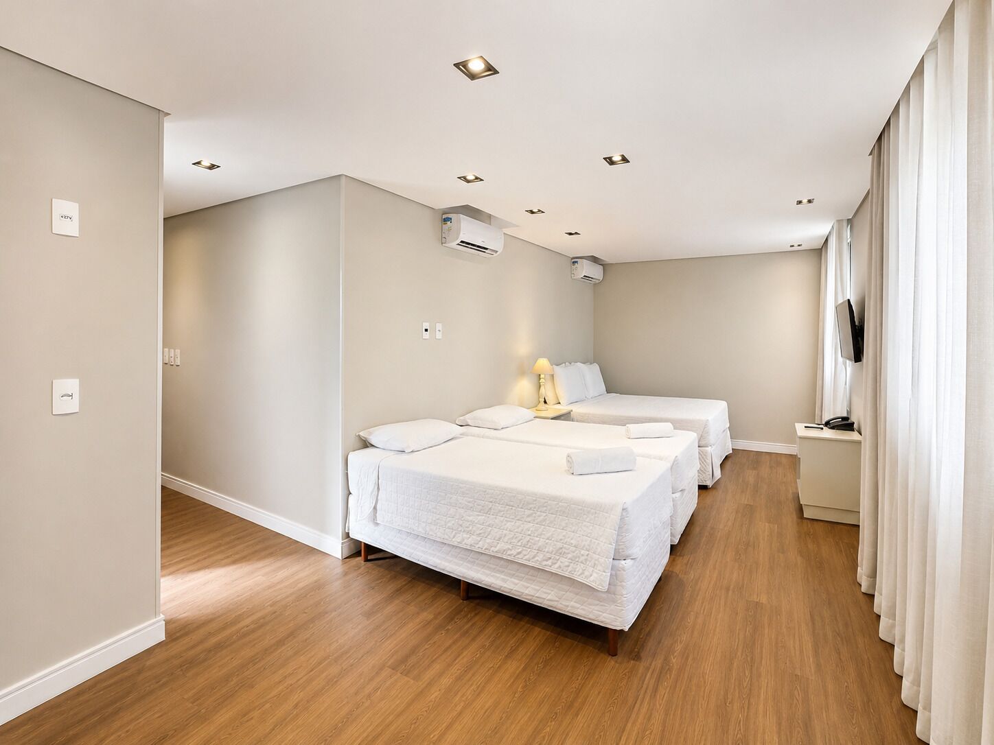 Habitación de hotel con dos camas, un televisor de pantalla plana, un equipo de aire acondicionado y piso de madera.