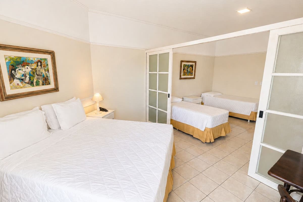 Une chambre d’hôtel avec un grand lit, deux petits lits, un bureau et une chaise.