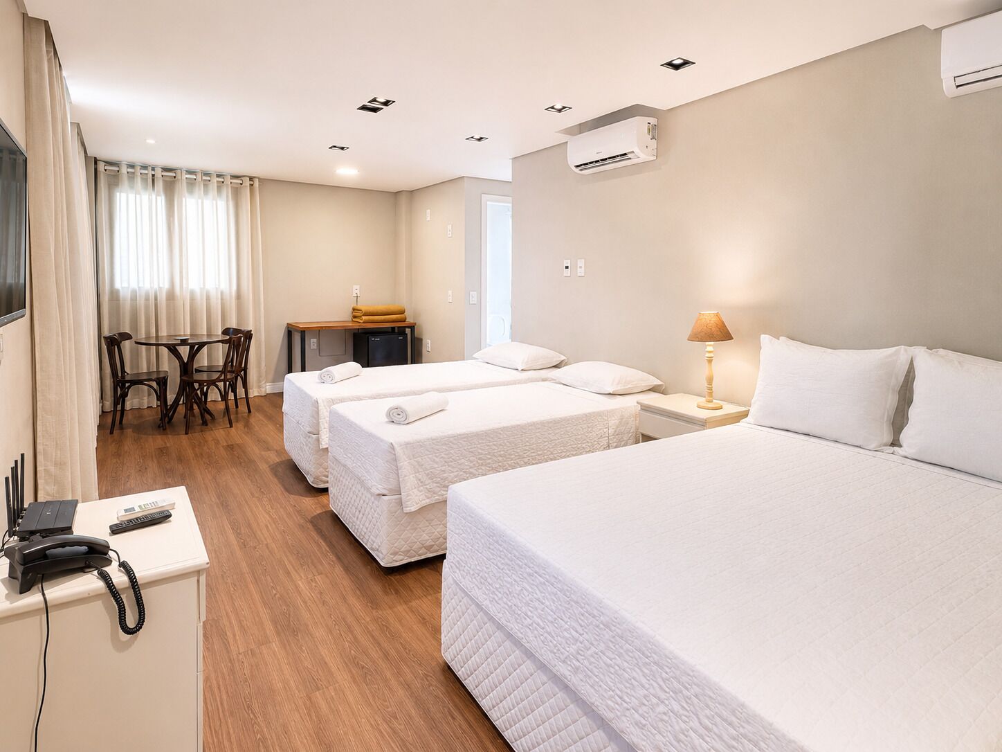 A hotel room with two beds, a desk, a chair, a telephone, and an air conditioning unit.