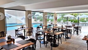 An outdoor dining area with tables and chairs, a pool, and umbrellas. - Hotel Praia Brava (Florianópolis)