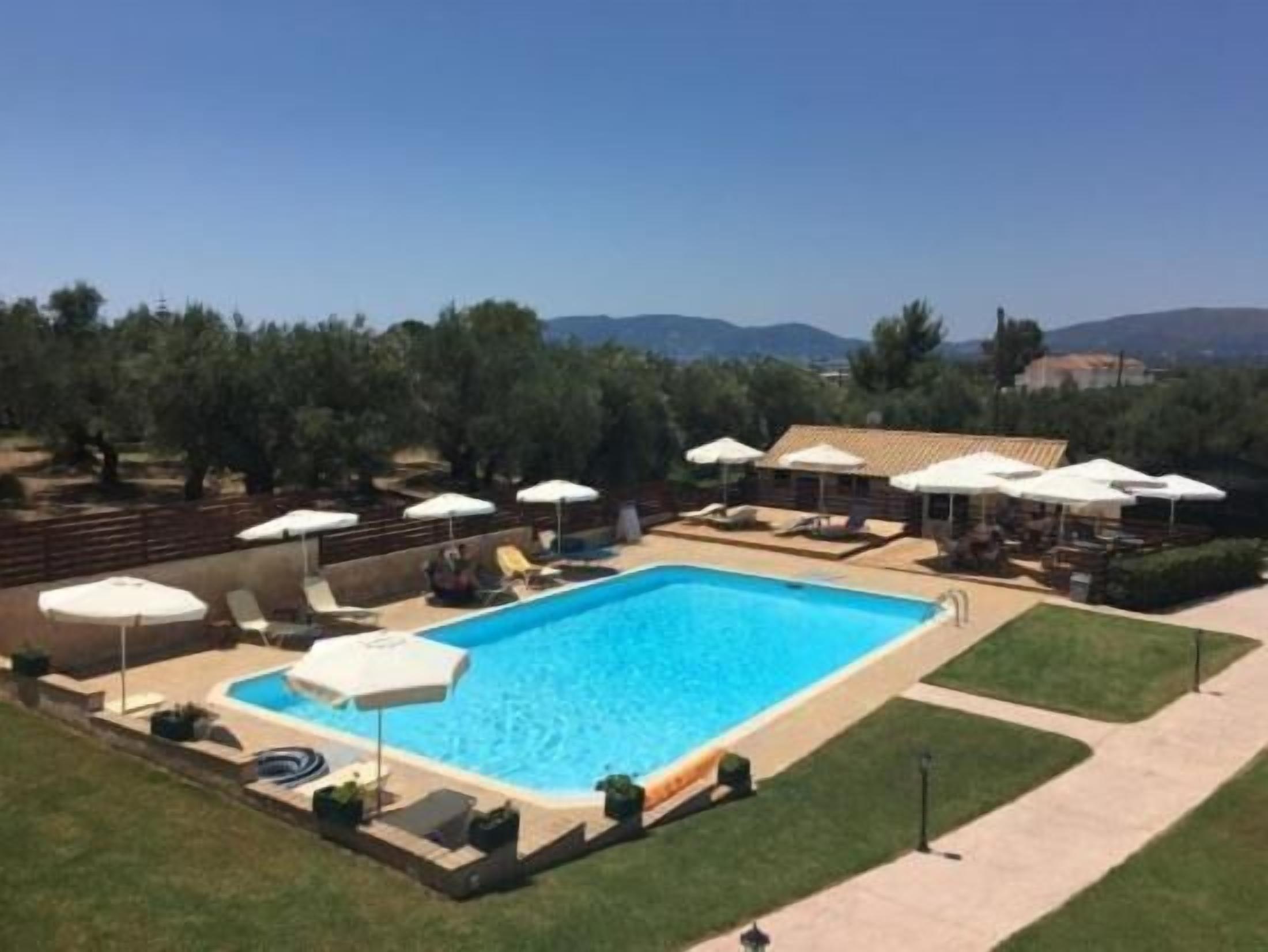 A rectangular swimming pool with lounge chairs and umbrellas, surrounded by a landscaped garden and a wooden fence.