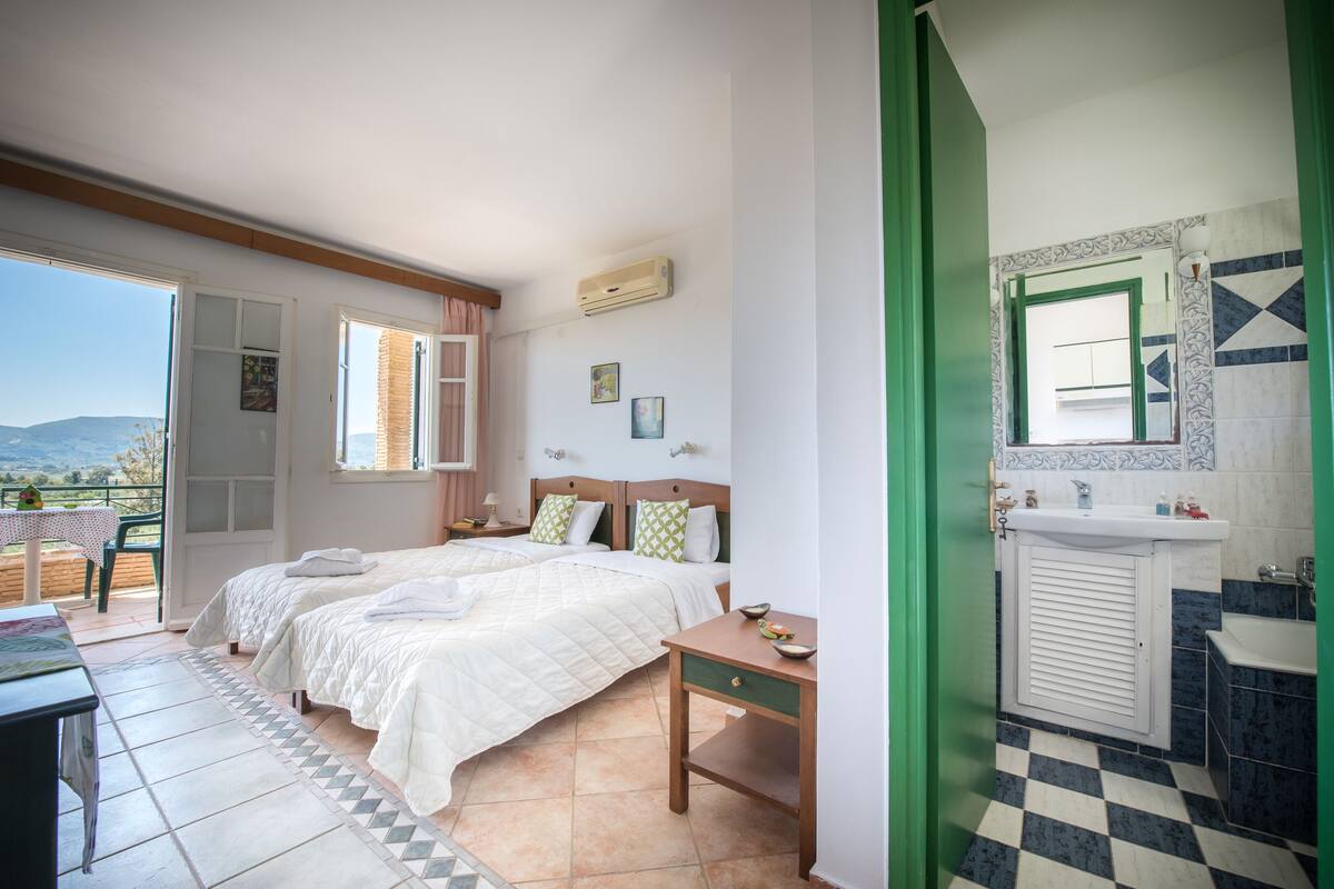 Un dormitorio con dos camas, una mesita, una mesita de noche y un baño con lavabo y espejo.