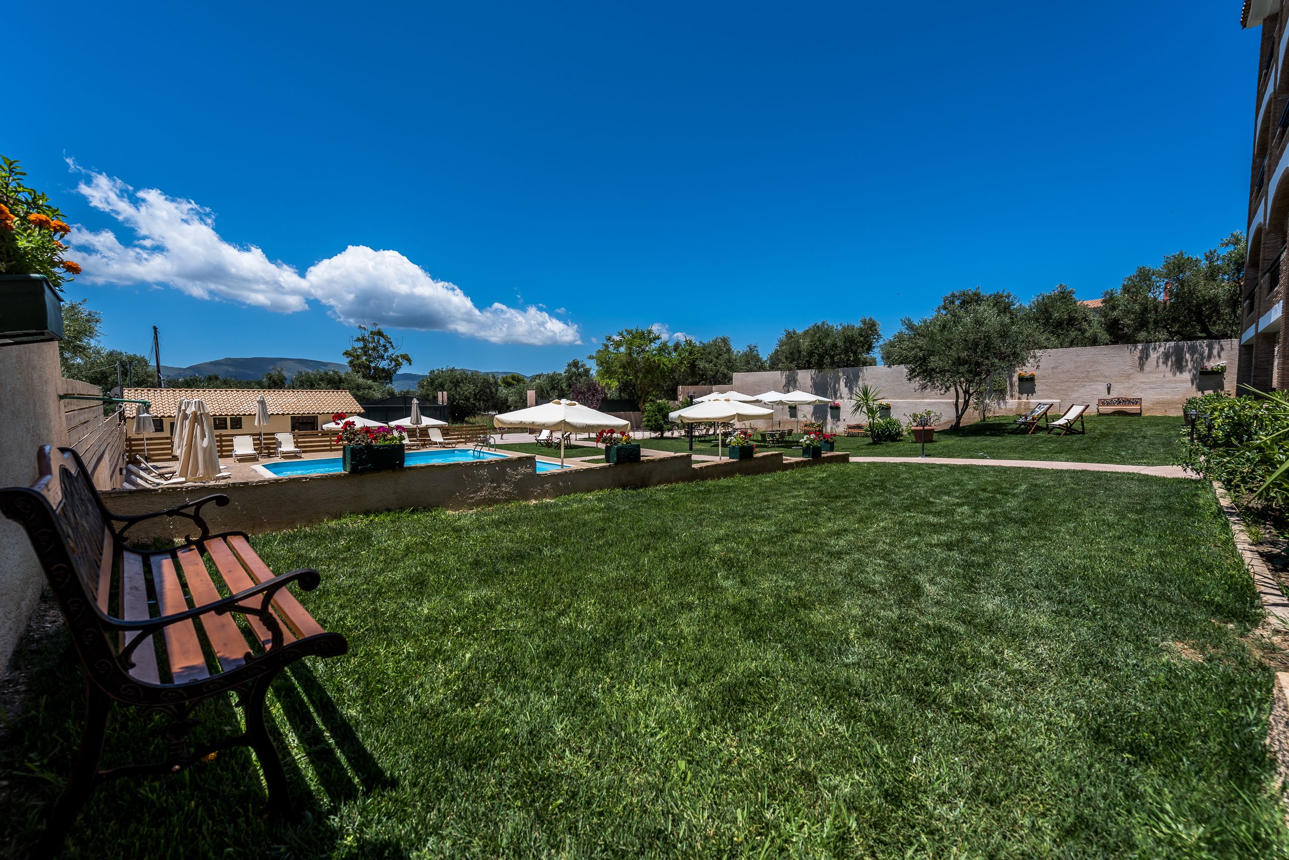 A pool area with a bench, umbrellas, and lounge chairs.