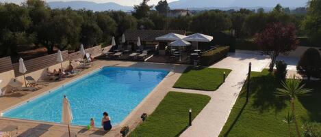 Una piscina amb gandules i ombrelles, envoltada per un pràctic jardí i vistes a muntanyes llunyanes.