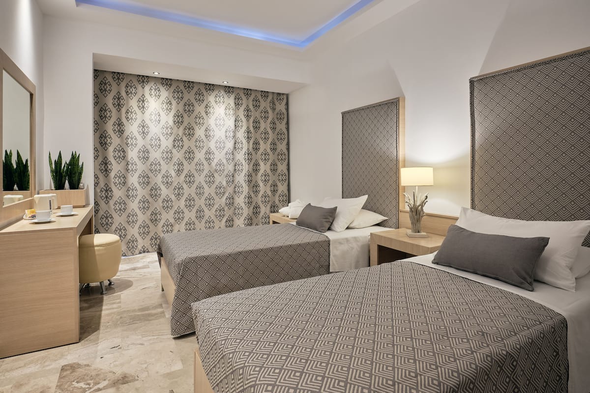 A modern hotel room with two beds, a desk, and a bathroom.