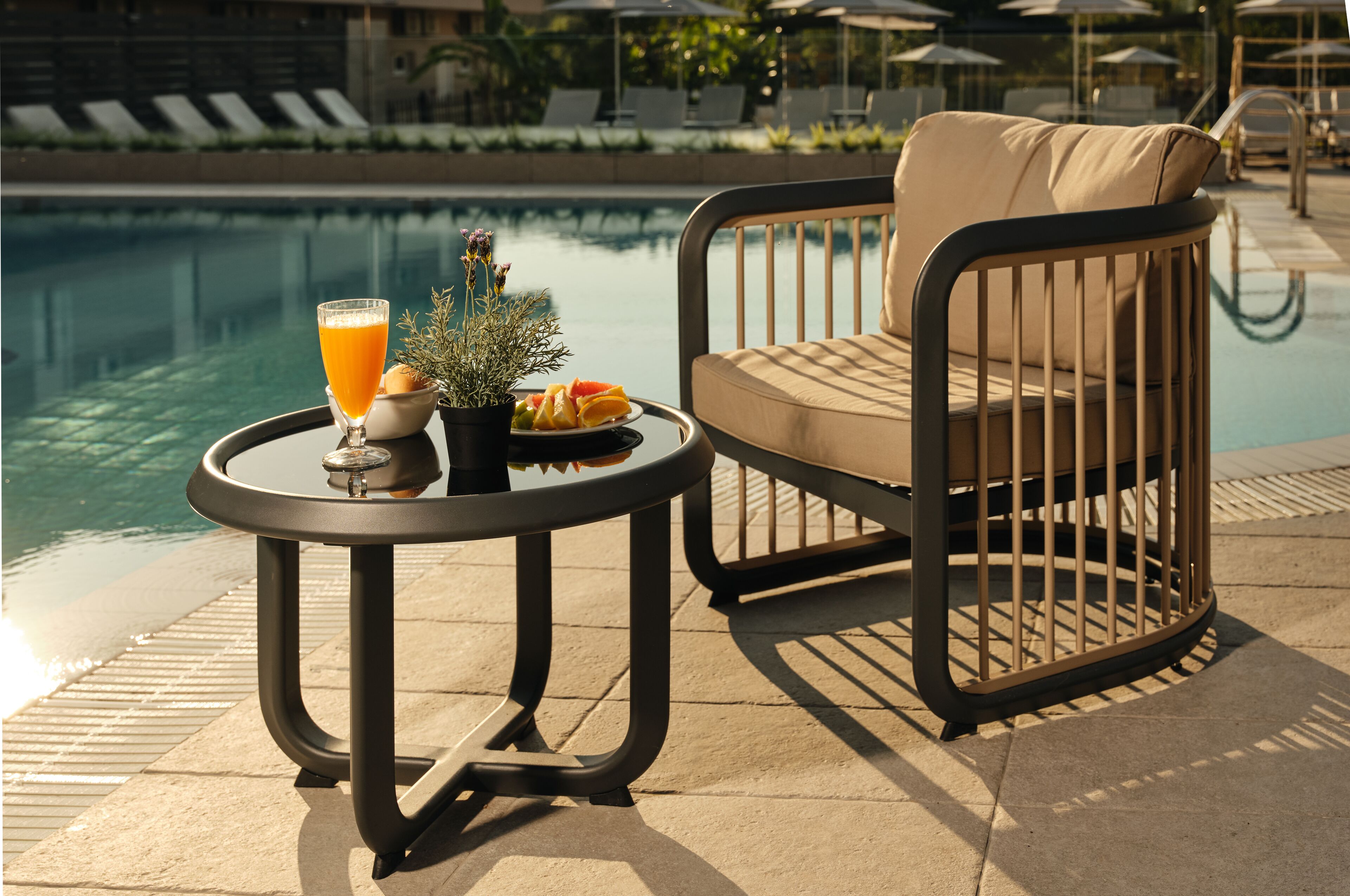 A poolside setting with a round table, a cushioned chair, and a glass of orange juice.