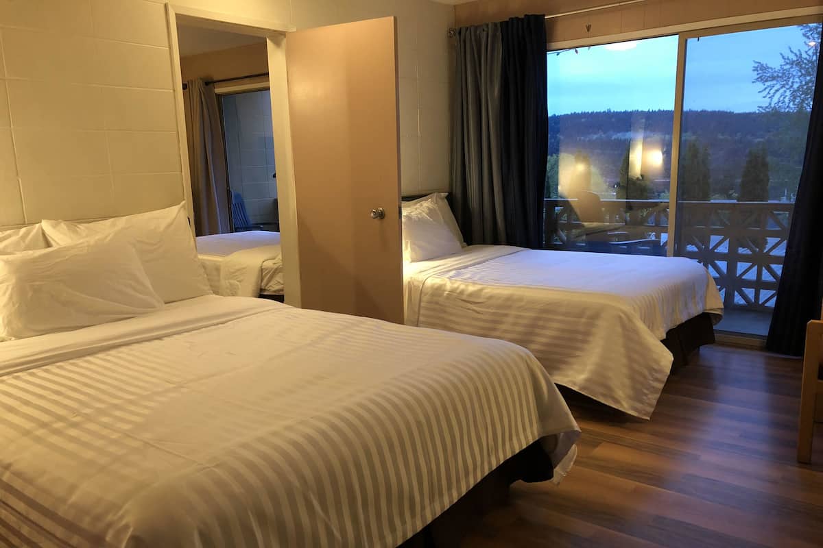 A hotel room with two beds, a balcony with a view of the forest, and a wooden floor.