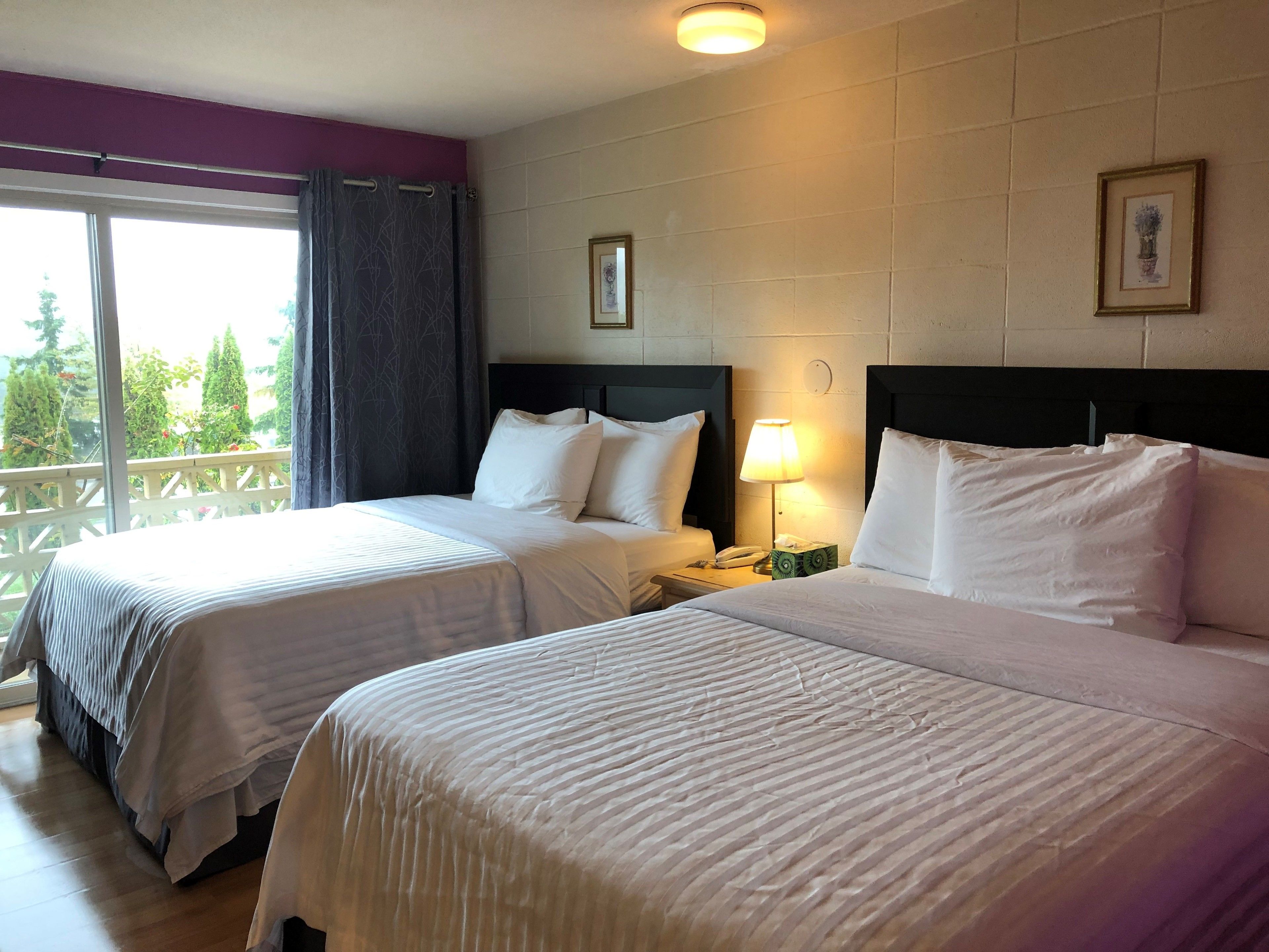Hotellihuone, jossa on kaksi sänkyä, parveke, yöpöytä lampun kanssa ja seinällä oleva kehystetty kuva.