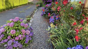 A residential property with a gravel pathway, vibrant flower beds, and a house with a balcony. - Holiday House Motel (Ladysmith)