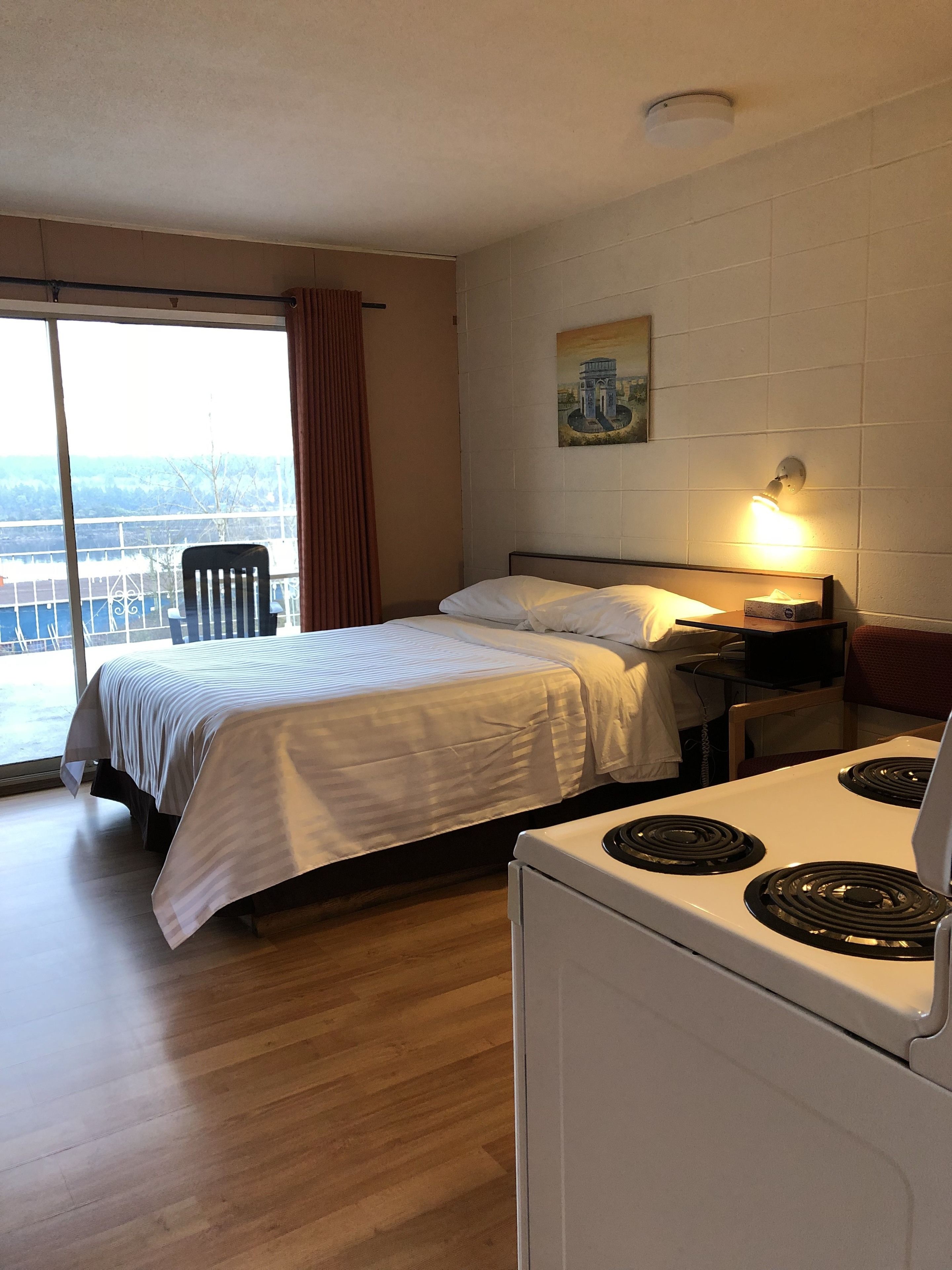 Une chambre d’hôtel avec un lit, un bureau doté d’une lampe, une cuisinière et une vue sur l’extérieur grâce à une grande fenêtre.