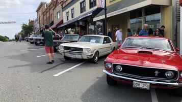 Una calle con autos antiguos estacionados a lo largo de la vereda, peatones caminando y comercios con letreros.